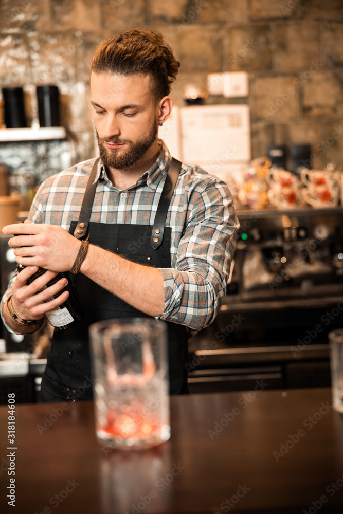 Young bearded bartender holding a bottle of alcohol