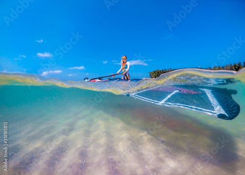 windsurfer girl with a board and a sail in tropical clear water, view from the waterline