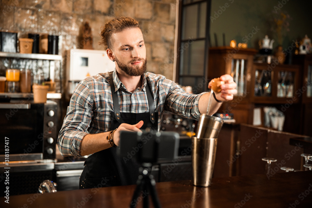 Smiling barman in apron using a cocktail shaker at bar