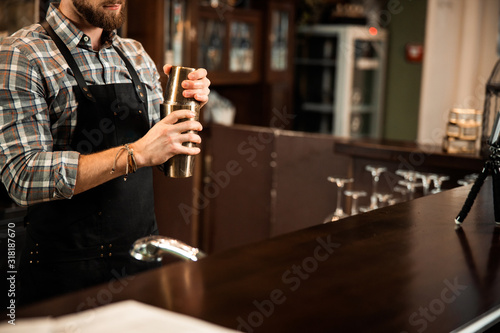 Young bartender making cocktail in shaker on bar counter