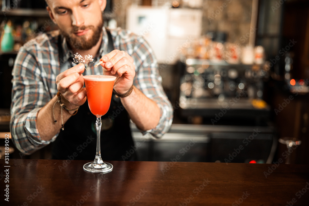 Young bearded bartender decorating glass of drink