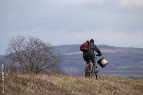 Homeless man with backpack driving bike and carry a bucket. Man traveling through the nature with his bicycle on cloudy day.