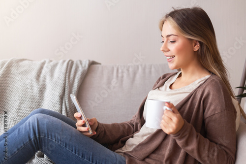 Cheerful woman with coffee chatting on cellphone at home