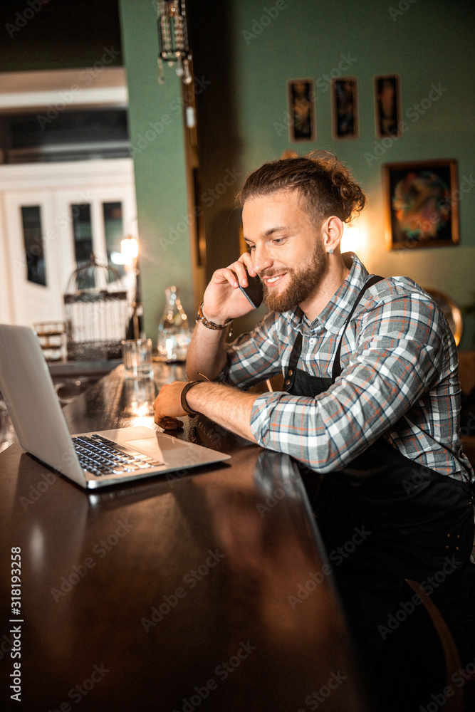 Smiling young barman is talking on smartphone Smiling young barman is talking on smartphone