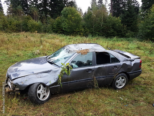 A battered gray car sedan lies in a roadside ditch among the lush green foliage of the bush in the summer. Road traffic incident. The consequences of speeding and the threat of life. Traffic safety
