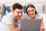 Couple Using Laptop Lying In Bed Watching Movie At Home