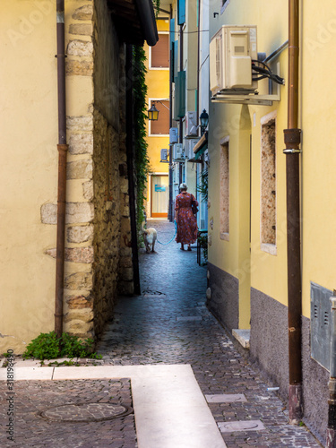 A woman walking a dog on a very narrow street between yellow buildings