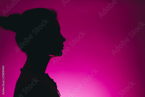 dark silhouette of a woman profile isolated on a pink background with copy space
