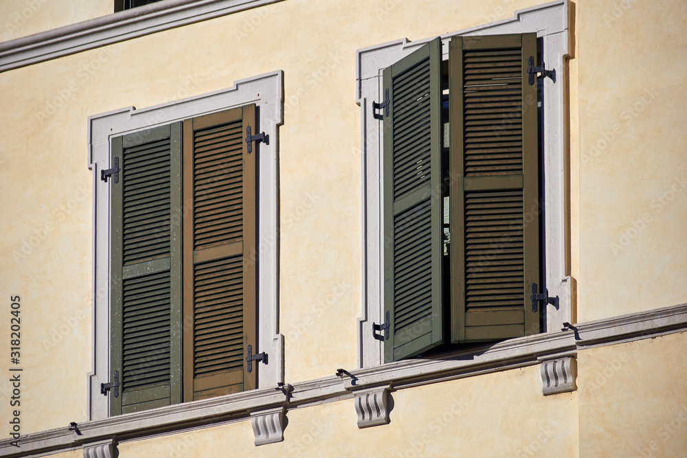 Two italian windows on the bright wall facade with closed wooden green shutters