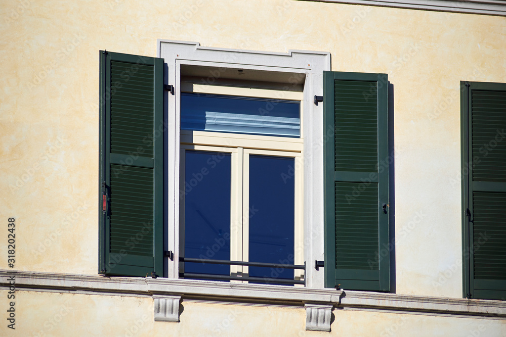 Italian window on the bright wall facade with open wooden green shutters