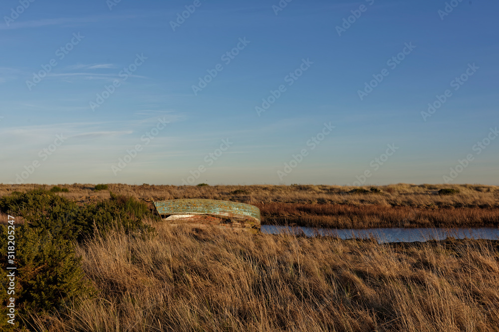 An abandoned Old Wooden Fishing Boat on the banks of a small Estuary under a clear blue sky and golden light of a Winters evening.