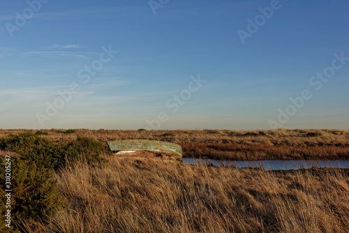 An abandoned Old Wooden Fishing Boat on the banks of a small Estuary under a clear blue sky and golden light of a Winters evening.
