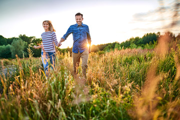 Joyful couple running through meadow on sunny summer day