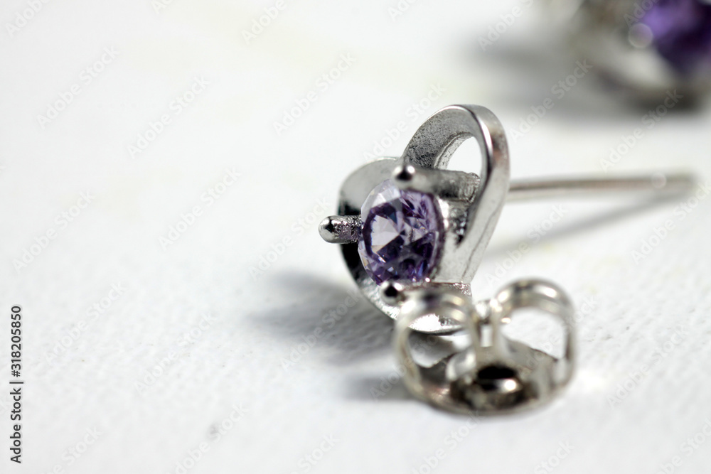 Close ups shot of white golden heart shaped ear stud with purple crystals gem Close ups shot of white golden heart shaped ear stud with purple crystals gem