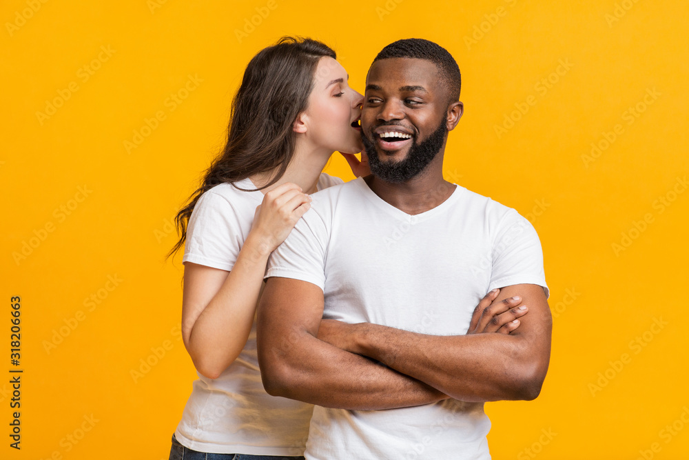 Obraz premium Romantic woman whispering about love into her black boyfriend's ear