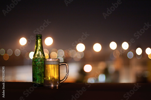 An empty bottle of beer and a glass of beer on a night city lights background