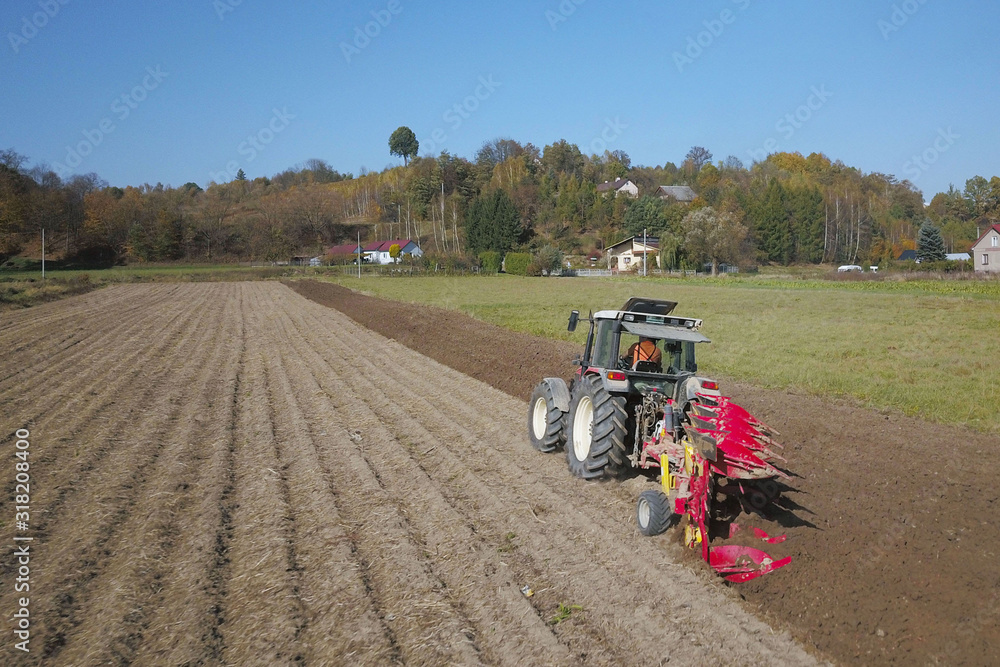 Obraz premium A farmer on a red tractor with a seeder sows grain in plowed land in a private field in the village area. Mechanization of spring field work. Farmer's everyday life. Processing of land. The agrarian