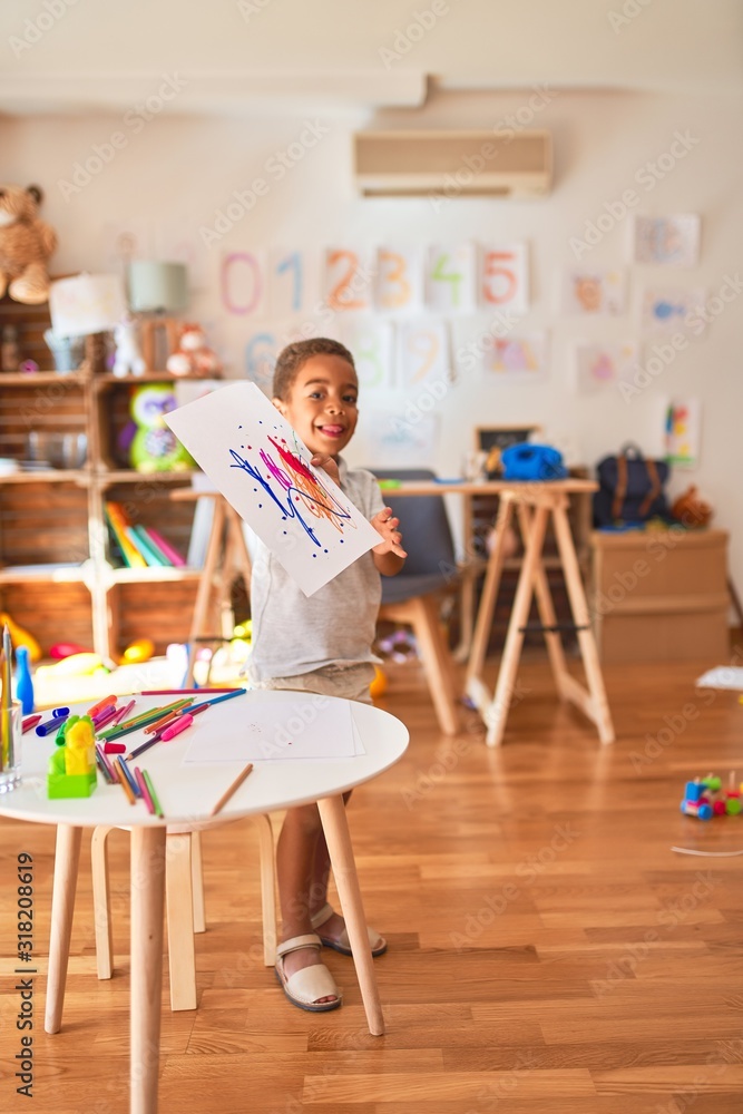 Beautiful african american toddler standing holding draw smiling at kindergarten Beautiful african american toddler standing holding draw smiling at kindergarten