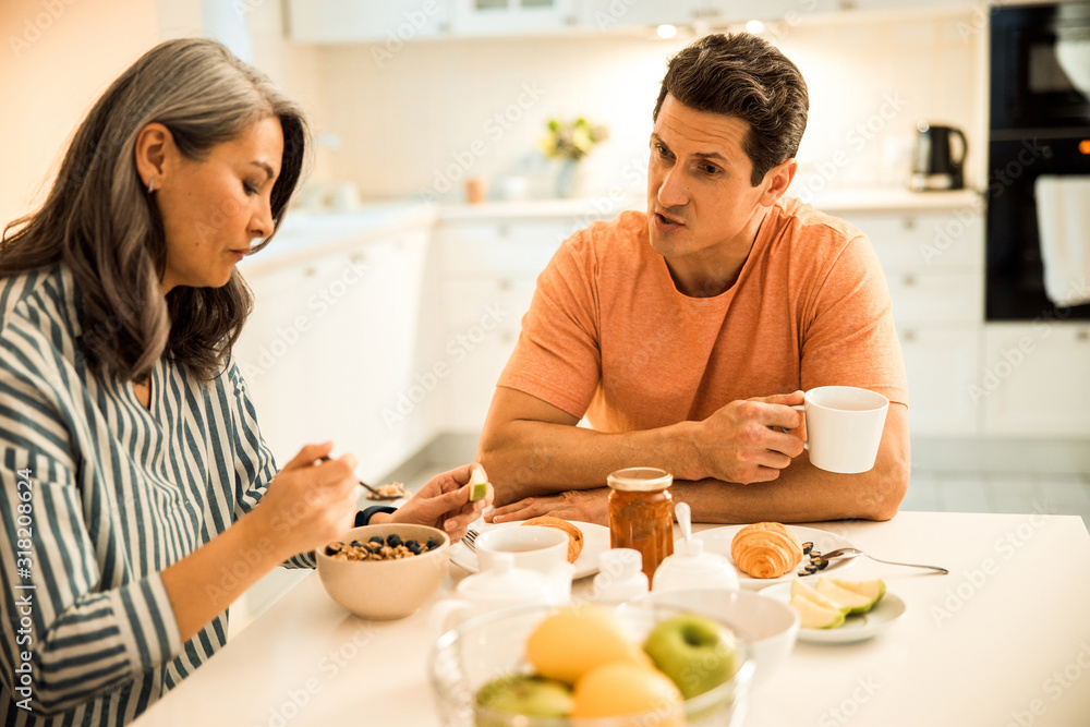 Smiling mature husband holding cup of tea and talking with wife Smiling mature husband holding cup of tea and talking with wife
