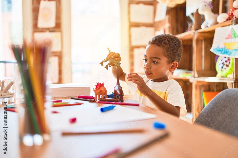 Beautiful african american toddler playing with dinosaurs toy on desk at kindergarten - obrazy, fototapety, plakaty 