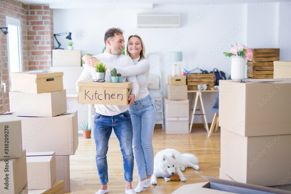 Fototapeta premium Young beautiful couple with dog moving cardboard boxes at new home