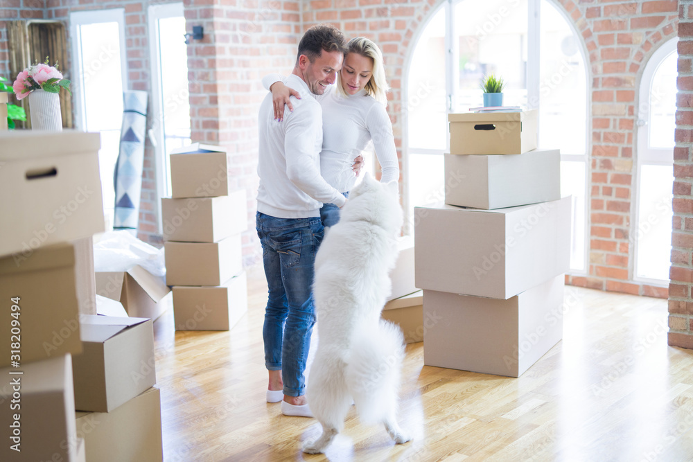 Young beautiful couple with dog hugging at new home around cardboard boxes Young beautiful couple with dog hugging at new home around cardboard boxes