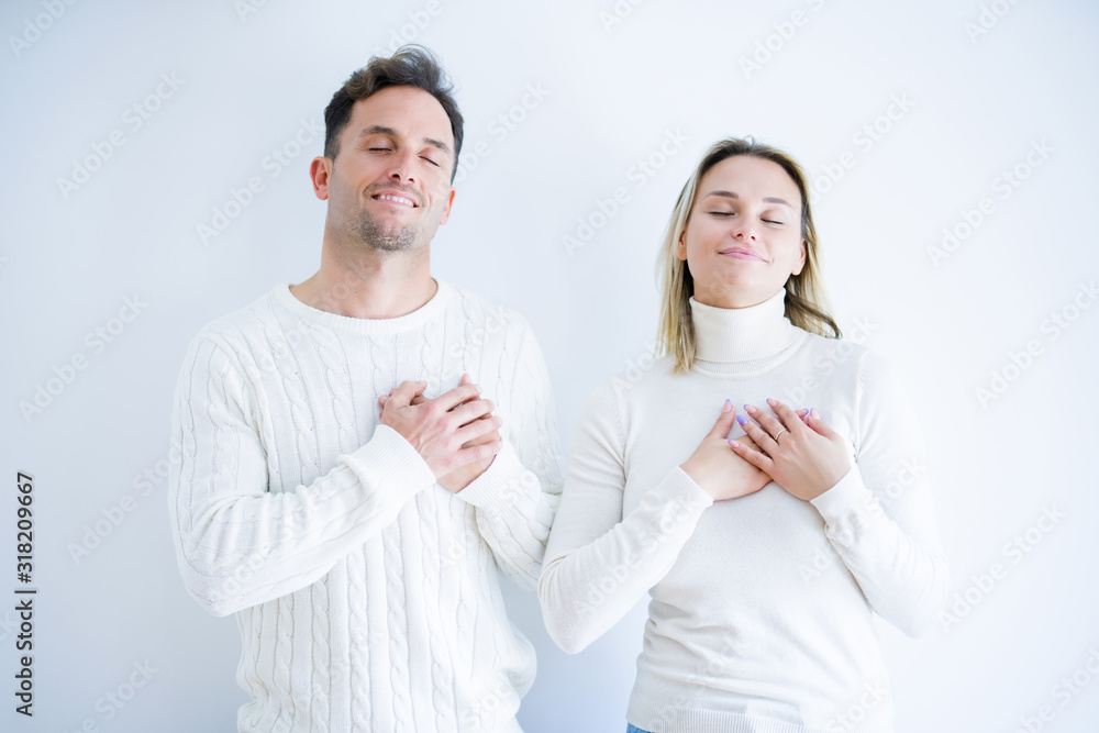Young beautiful couple wearing casual t-shirt standing over isolated white background smiling with hands on chest with closed eyes and grateful gesture on face. Health concept. Young beautiful couple wearing casual t-shirt standing over isolated white background smiling with hands on chest with closed eyes and grateful gesture on face. Health concept.