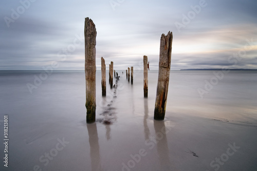 Holzstangen am Ostseestrand im Abendlicht, Wasserbewegung in Langzeitbelichtung, stille melancholische Stimmung, Blickführung mit Tiefenwirkung durch die Anordnung der Hölzer - Ostsee, Insel Rügen photo