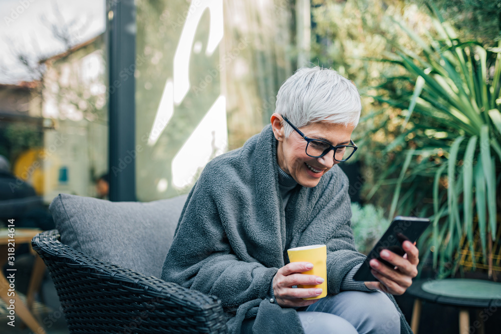 Portrait of a cheerful senior woman using mobile phone while sitting in the garden. Portrait of a cheerful senior woman using mobile phone while sitting in the garden.