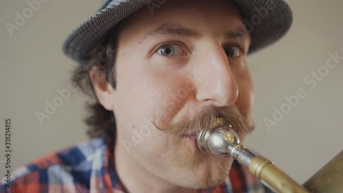 Cheerful young man with a funny mustache and a hat playing on the big tuba. Close up