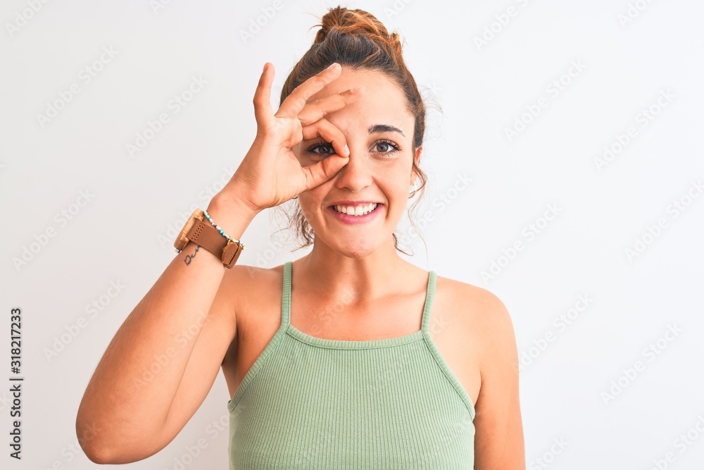 Young redhead woman wearing a bun over isolated background doing ok gesture with hand smiling, eye looking through fingers with happy face. Young redhead woman wearing a bun over isolated background doing ok gesture with hand smiling, eye looking through fingers with happy face.