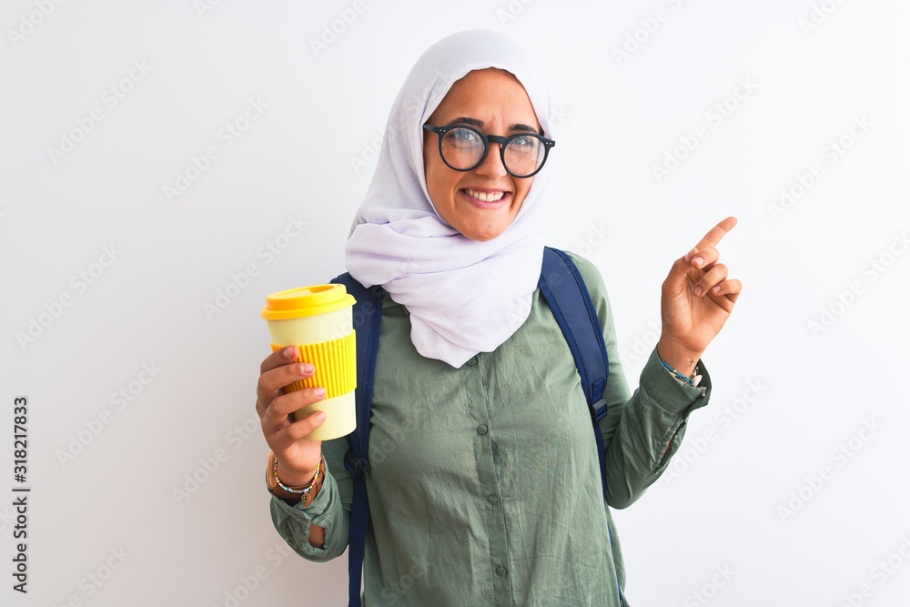 Young Arab student woman wearing hijab and drinking coffee over isolated background very happy pointing with hand and finger to the side Young Arab student woman wearing hijab and drinking coffee over isolated background very happy pointing with hand and finger to the side