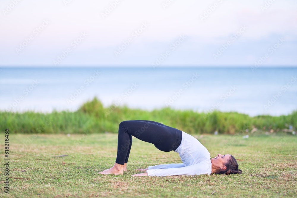 Fototapeta premium Young beautiful sportwoman practicing yoga. Coach teaching bridge pose at park