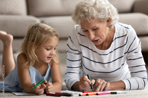 Old senior woman teaching small granddaughter coloring images.