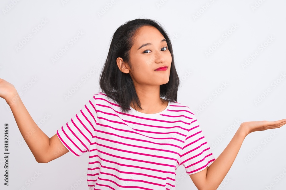 Young chinese woman wearing striped t-shirt standing over isolated white background clueless and confused expression with arms and hands raised. Doubt concept. Young chinese woman wearing striped t-shirt standing over isolated white background clueless and confused expression with arms and hands raised. Doubt concept.