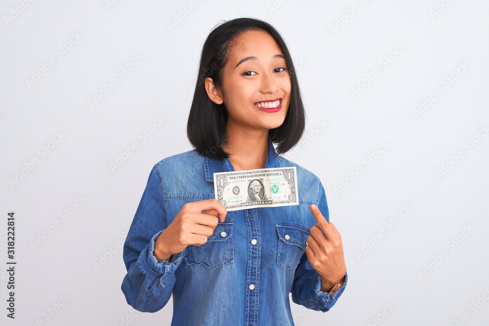 Young beautiful chinese woman holding one dollar standing over isolated white background very happy pointing with hand and finger Young beautiful chinese woman holding one dollar standing over isolated white background very happy pointing with hand and finger