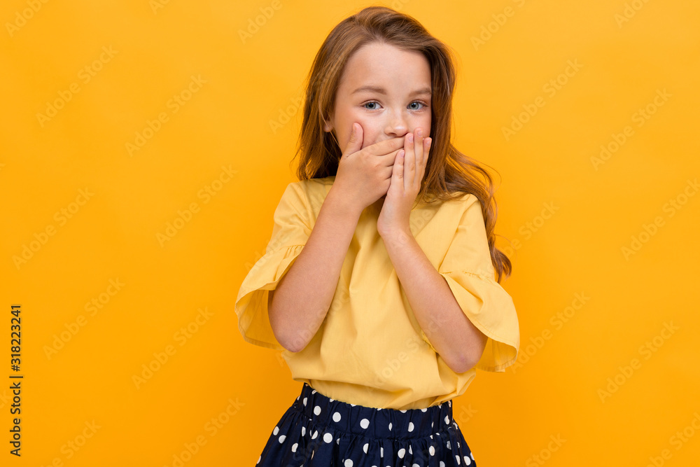 stylish charming young girl in a light yellow blouse and a dark skirt covered her mouth with her hands on a yellow background stylish charming young girl in a light yellow blouse and a dark skirt covered her mouth with her hands on a yellow background