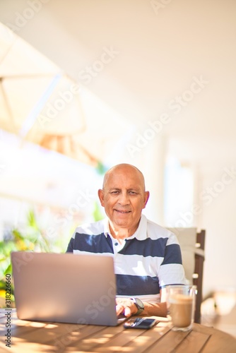 Senior handsome man smiling happy and confident. Sitting using laptop at terrace