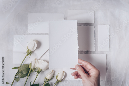 Wedding mockup. Flowers composition. White paper, elegand hand holding card, roses on white textile background. Valentine's Day. Flat lay, top view, copy space photo