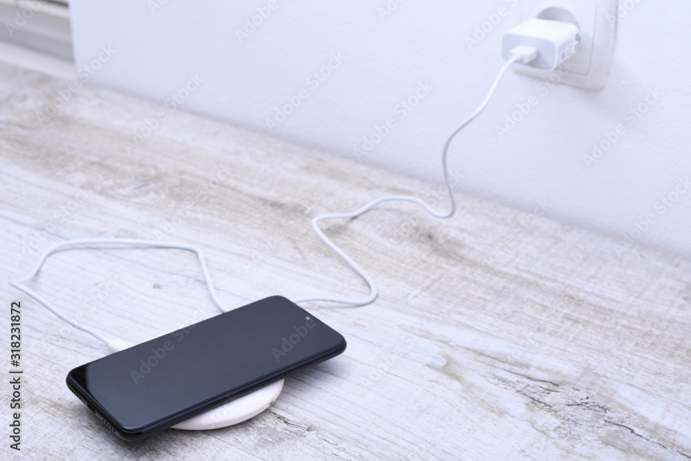 Mobile phone charge on a wireless charger, modern equipment concept on a wooden table background Mobile phone charge on a wireless charger, modern equipment concept on a wooden table background