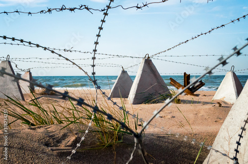 barbed wire and concrete military fence on the beach near the sea in Crimea © Sofiia