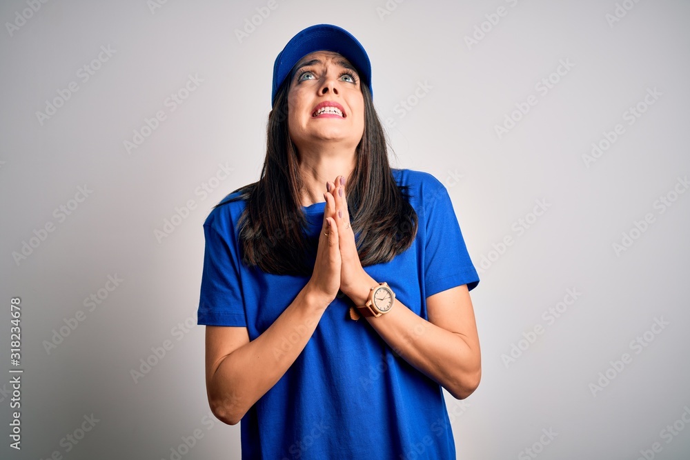 Young delivery woman with blue eyes wearing cap standing over blue background begging and praying with hands together with hope expression on face very emotional and worried. Begging. Young delivery woman with blue eyes wearing cap standing over blue background begging and praying with hands together with hope expression on face very emotional and worried. Begging.
