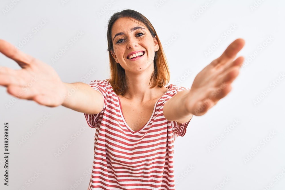 Beautiful redhead woman wearing casual striped red t-shirt over isolated background looking at the camera smiling with open arms for hug. Cheerful expression embracing happiness. Beautiful redhead woman wearing casual striped red t-shirt over isolated background looking at the camera smiling with open arms for hug. Cheerful expression embracing happiness.