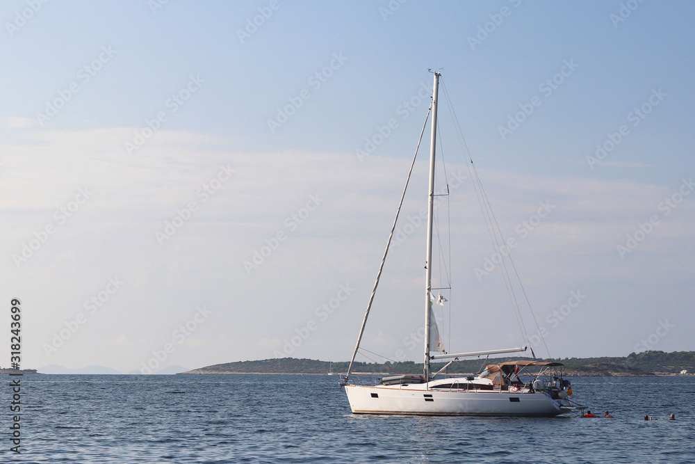 A modern sailing yacht is anchored in a bay. People bathe in the sea. Active rest on the Adriatic Sea of the Mediterranean region. Dalmatian riviera of Croatia. Prestigious and rich lifestyle A modern sailing yacht is anchored in a bay. People bathe in the sea. Active rest on the Adriatic Sea of the Mediterranean region. Dalmatian riviera of Croatia. Prestigious and rich lifestyle