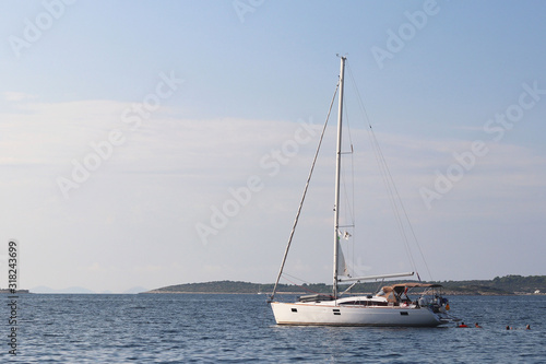 A modern sailing yacht is anchored in a bay. People bathe in the sea. Active rest on the Adriatic Sea of the Mediterranean region. Dalmatian riviera of Croatia. Prestigious and rich lifestyle © Xato Lux