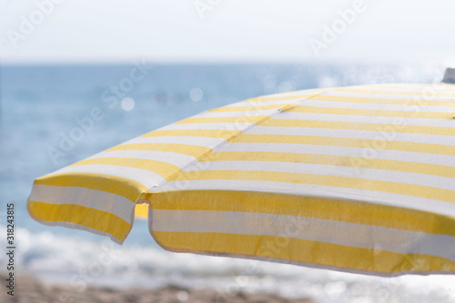umbrella with yellow stripes over a deck chair on the beach, against the sea with sun glare