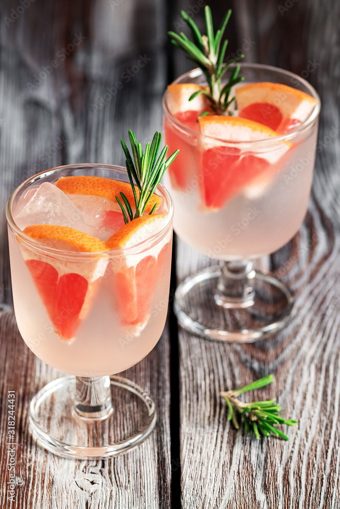 Refreshing drink with grapefruit and rosemary in a glass on a wooden rustic table. Selective focus. Summer cold beverage. Refreshing drink with grapefruit and rosemary in a glass on a wooden rustic table. Selective focus. Summer cold beverage.