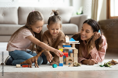 Young mom playing with building bricks with little daughters