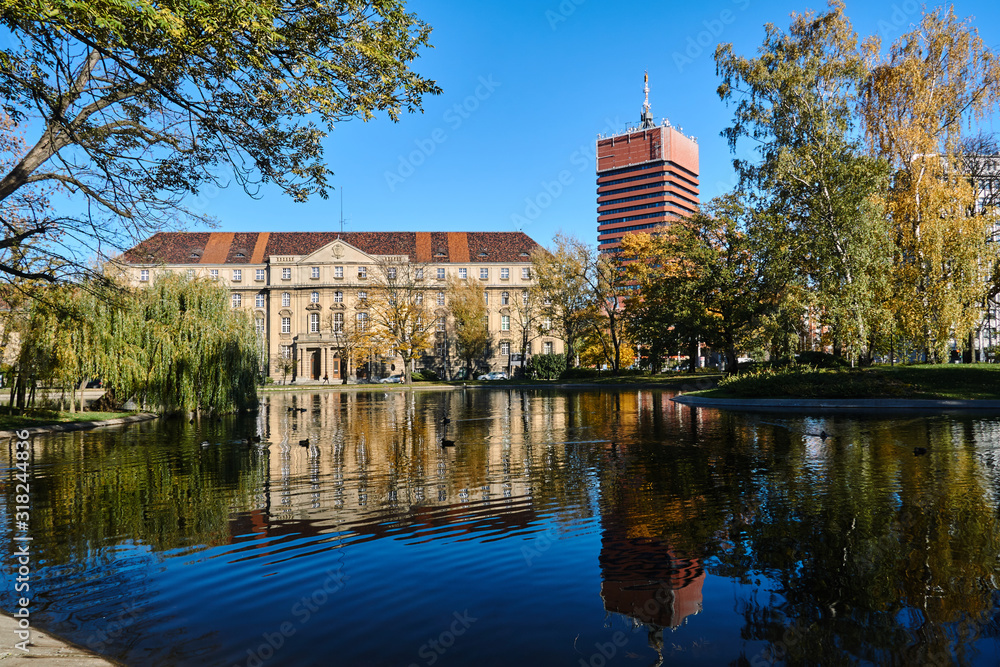 Obraz premium Trees on a pond in a park and a modern buildings in Poznan.