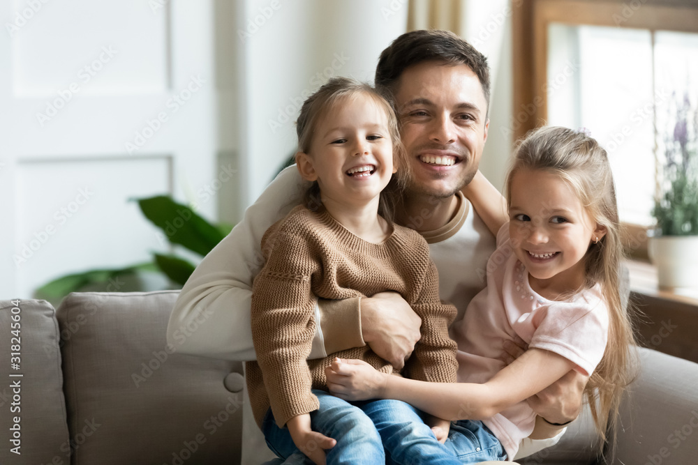 Fototapeta premium Happy dad cuddle little daughters relaxing together at home
